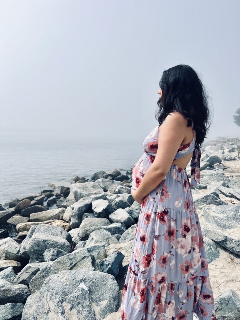 Pregnant women in a dress holding her belly near the shore